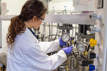 A researcher handles a pressure vessel reactor in a fumehood
